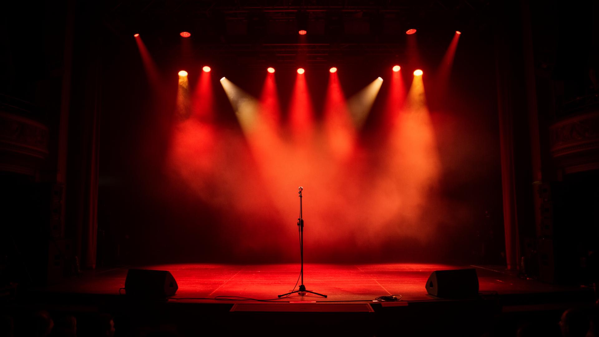 Solo acoustic performer under warm amber stage spotlight in front of a crowd silhouette